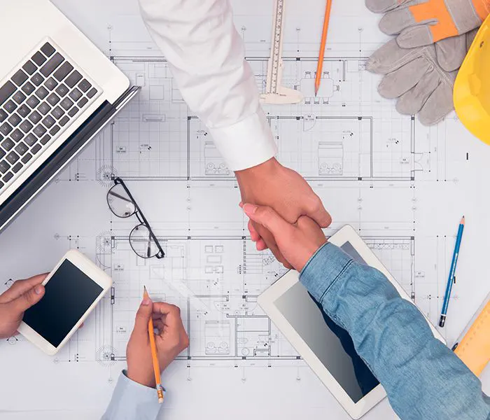 Business professionals shaking hands over architectural blueprints, symbolizing local agent supports and collaboration in construction and real estate project services